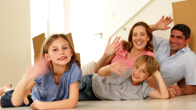 Happy family lying on floor in their new home waving at camera