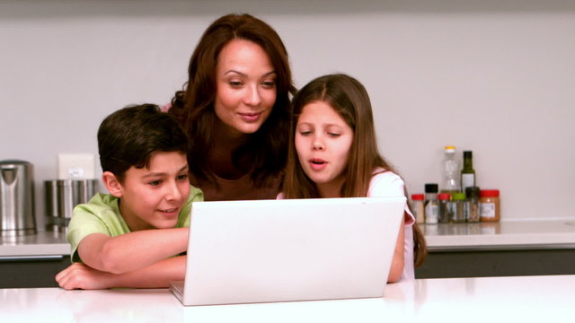 Mother using laptop with her children in kitchen