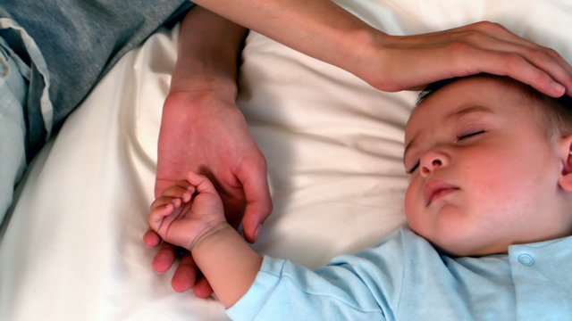 Mother lying with sleeping baby boy on bed