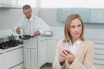 Fototapeta premium Businesswoman text messaging while man preparing food in kitchen