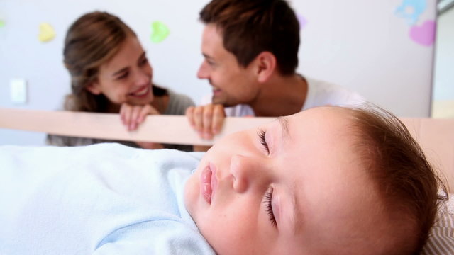 Happy parents watching over baby son in crib