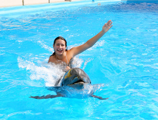 Happy beautiful young girl laughs and swims with dolphins in blu
