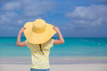 Fototapeta na wymiar Rear view of little girl in a big yellow straw hat on white sand