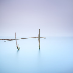 Poles and soft water on foggy landscape. Long exposure.