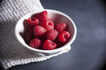 Fresh red raspberries in white bowl with moody lighting