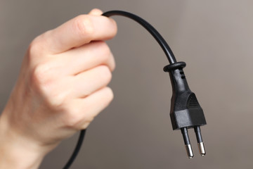 Hand holding electric plug on grey background
