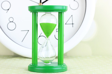 Hourglass and big clock on light background