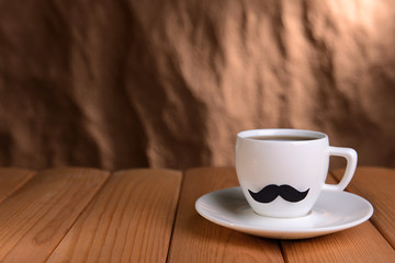 Cup with mustache on table on brown background