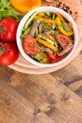 Beef salad in bowl with vegetables and spices on wooden table