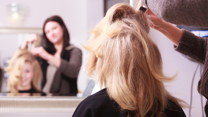 Smiling girl with blond wavy hair by hairdresser in beauty salon