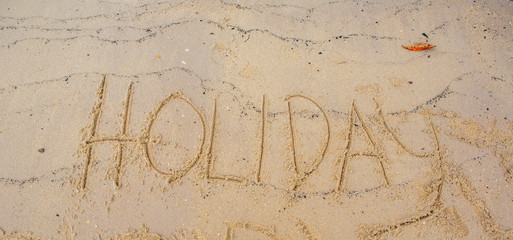 Beach with the word HOLIDAY scribbled on the sand 