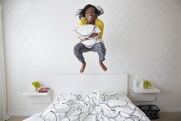 A young girl jumping high in the air above her bed.