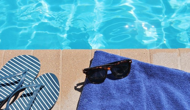 Poolside sunglasses towel holiday vacation background scenic sunglasses shoes with copy space on swimming pool water for vacation or holiday stock photo photograph image 