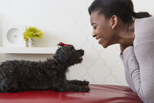 A young girl playing with her small black pet dog.
