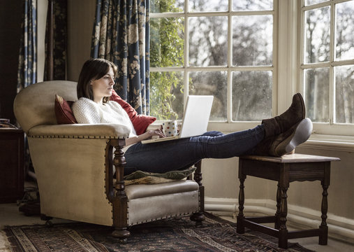 A young woman relaxing at home, with her feet up, using a laptop.