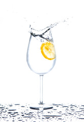 Lemon splashing into glass of water on white background