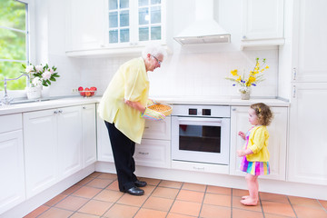 Happy grandmother and little girl cooking pie in white kitche