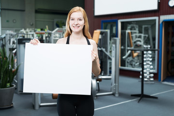 Frau im Fitnessstudio hält Werbetafel