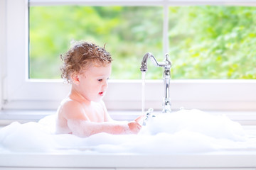 Sweet baby girl playing with water and foam in big kitchen sink