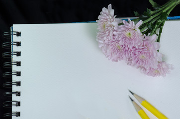 A white sketchbook, had and pink flower on black cloth