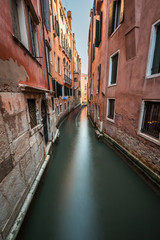 Fototapeta na wymiar Narrow Canal Among Old Colorful Brick Houses in Venice, Italy