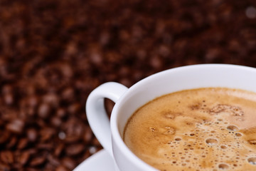 white cup of coffee on a background of coffee beans