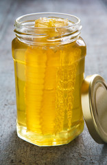 Jar Of Honey With Honeycomb On Wooden Surface