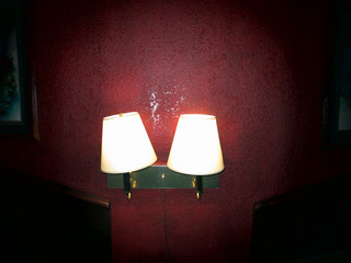 Old lamps lit on a red wall in an old motel room.