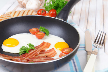 Scrambled eggs and bacon on frying pan on table close-up