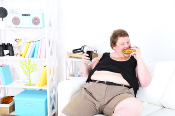 Fat man eating tasty sandwich and drink coke