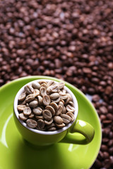 Cup full of green coffee beans on brown coffee beans background