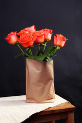 Beautiful roses in paper bag on wooden table on black