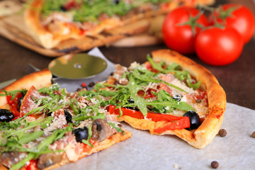 Pizza with arugula on cutting board, on color wooden background