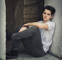 Attractive young man sitting on old door's threshold