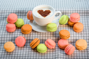 Colorful macaroons with cup of coffee with heart shape on the ch