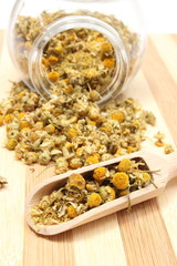 Dried chamomile in glass jar and on wooden spoon