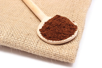 Ground coffee on wooden scoop lying on jute fabric