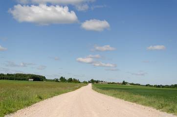 Fototapeta na wymiar gravel road continues along fields and blue sky