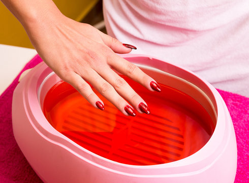 Female hand and orange paraffin wax in bowl.   