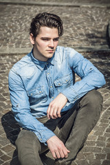 Attractive young man sitting on pavement outdoors