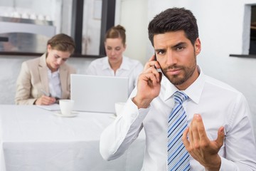 Businessman using mobile phone with colleagues at office desk