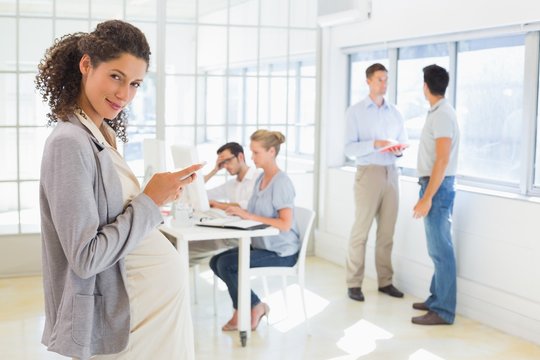 Pregnant businesswoman sending text with team behind her