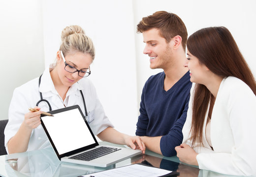 Doctor Showing Report To Couple On Laptop