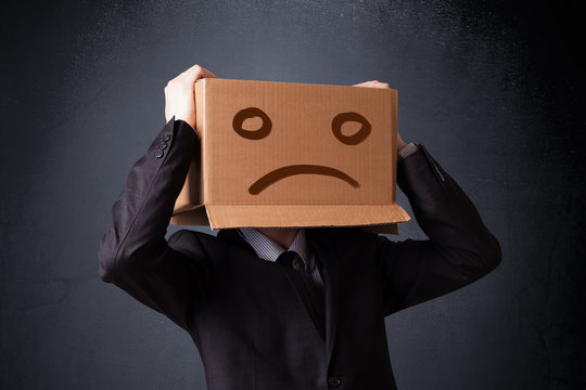 Businessman gesturing with cardboard box on his head with sad fa