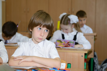 Portrait of schoolboy at workplace with another children in clas