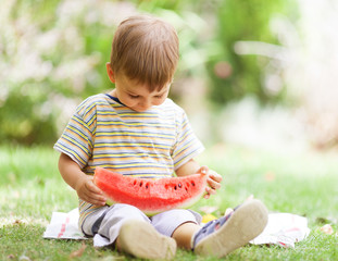 Cute little boy eating watermelon sitting on the grass.