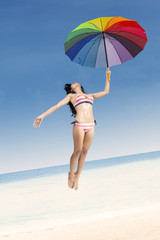 Fototapeta na wymiar Woman in stripeed bikini jumping with umbrella