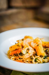 Italian pasta with shrimps and vegetables on wooden background