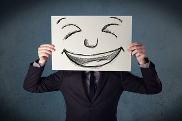 Businessman holding a paper with smiley face in front of his hea