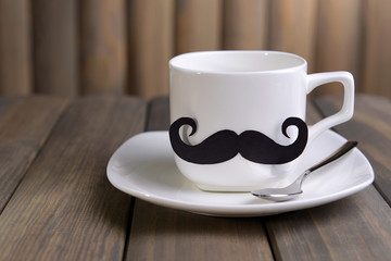 Cup with mustache on table on wooden background